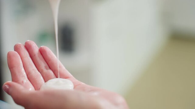 close-up hand receiving cream pour onto palm, smooth white lotion dispensed from bottle, gentle squeeze and glossy droplets, blurred bathroom counter background, skincare routine demo, moisturizing