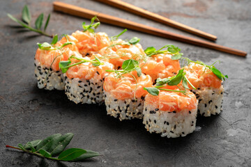 Luxurious salmon-topped sushi rolls with sesame-crusted rice, crowned with fresh salmon tartare and delicate microgreens on a dark slate backdrop. Premium Japanese fusion maki, gourmet seafood roll