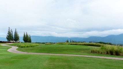 Landscape of green grass Lawn yard, golf course with a concrete walkway on lawn land, mountain in background under cloudy sky