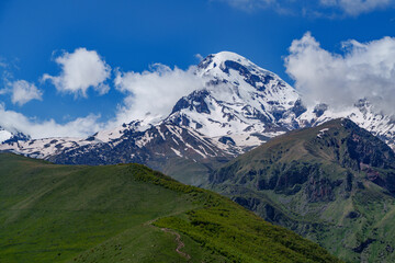 Fototapeta premium Mount Kazbek snowy summit above rolling green hills