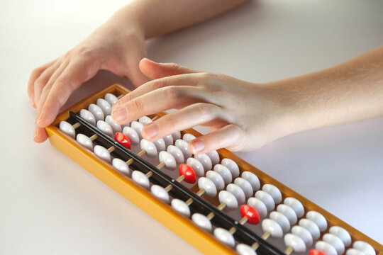 Hands using a yellow abacus with white and red beads on a clean white surface, illustrating traditional counting, learning, and math education concepts.