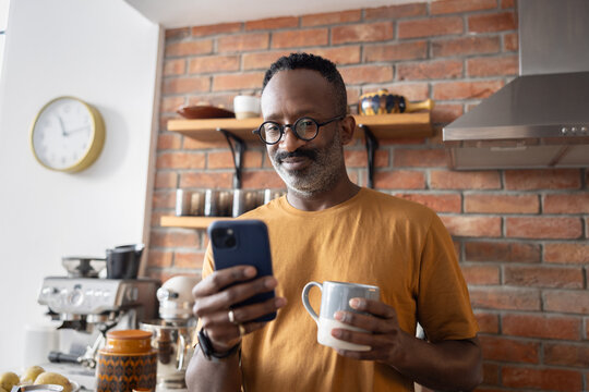 Man smiling while checking phone and holding mug