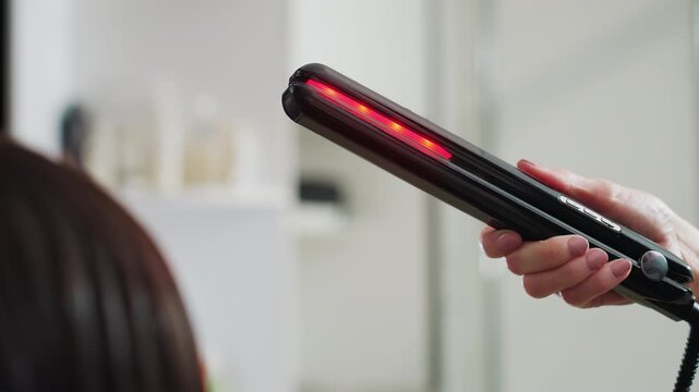 caucasian stylist holding heated straightener hovering above wet hair, glowing plates framed over client head, salon lighting and mirror reflections, careful technique and safety focus