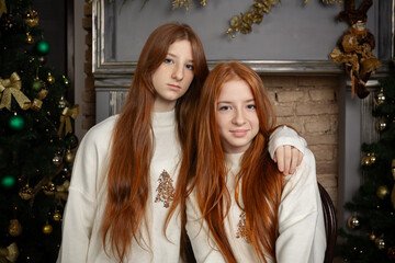 Two young women with long red hair wearing white Christmas sweaters