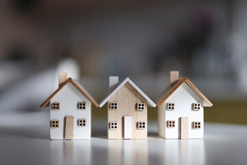 Three miniature model houses with wooden roofs on a white surface