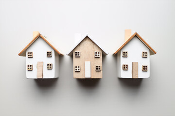 Three miniature wooden houses with white facades and brown roofs on a gray background