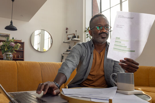 Concentrated Man Reviewing paperwork with Laptop Nearby
