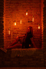 A young woman with red hair poses in moody, industrial lighting