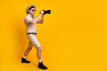 Adventurous photographer in safari outfit shoots with camera against bright yellow background