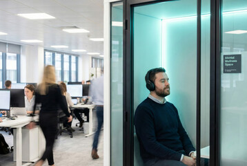 A man relaxes in a cozy booth wearing headphones promoting mental health at work