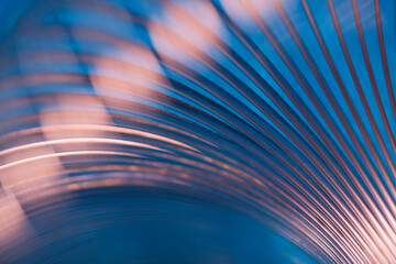 Abstract industrial metal background with curved steel lines on blue. Shiny spiral spring texture with pink reflections for hardware manufacturing presentation. Photo