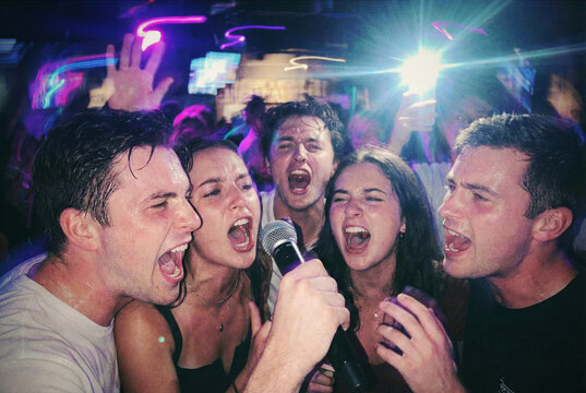 A group of young people sings passionately into a microphone during a lively night out