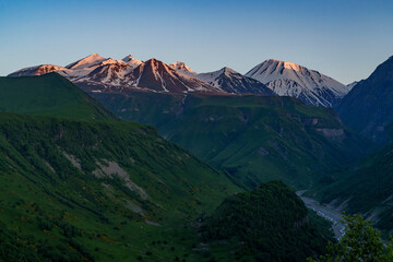 Sunset light on snowy Caucasus peaks above green river valley