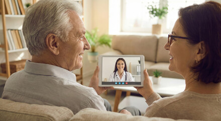Elderly couple smiles while consulting a doctor on a tablet at home during the day