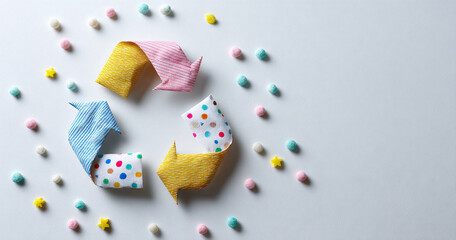 Colorful fabric arrows arranged in a recycling symbol surrounded by small pastel pom-poms and yellow star shapes on a light background