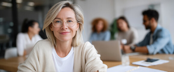 Confident businesswoman with glasses smiling at camera in modern with diverse colleagues working in background