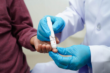 Asian senior woman using lancet pen on senior patient finger for check sample blood sugar level to treatment diabetes.
