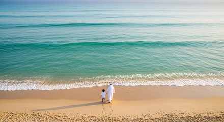 Arab father and son walk hand-in-hand on a beautiful sandy beach by the turquoise sea leaving footprints