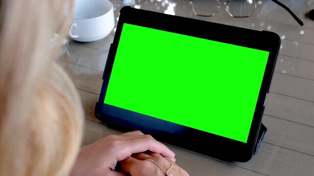 A woman has a blank green screen on her tablet. A woman using a tablet computer with a green screen.