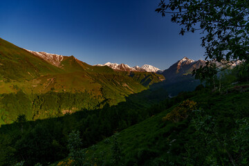 Snowy Caucasus peaks above deep green forested valley at sunrise