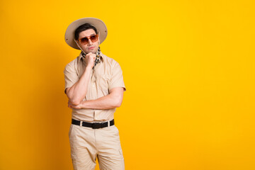 Man in safari outfit with hat and sunglass poses against a bright yellow background for travel...