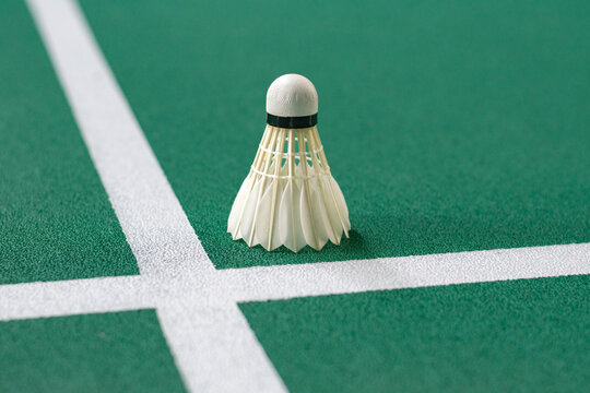 A white shuttlecock sits perfectly on the intersection of the two white service lines, sharply contrasting with the deep green texture of the badminton court surface.