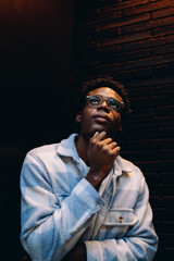 Contemporary portrait of a young man thoughtfully looking upwards with his hand under chin. A metaphorical expression of hope, innovation, and creative thinking in modern tech-driven culture.