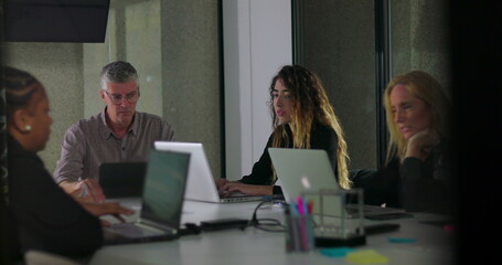 Obraz premium Focused business team working on laptops during quiet office meeting with diverse colleagues seated around table in modern workspace