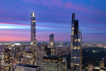 The dramatic verticality of New York City Billionaires Row towers illuminated against a vibrant evening sky, with the urban sprawl extending below.