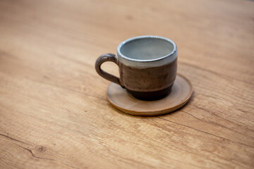 Obraz premium Handmade ceramic coffee cup with saucer on a wooden table. Simple clay design with glazed surface.
