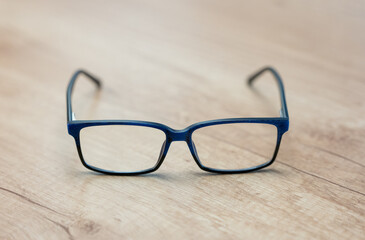 Blue rectangular eyeglasses on a wooden table. Modern, lightweight frame suitable for daily wear, reading or screen use—ideal for eyewear advertising and product display.