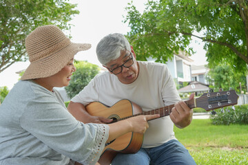 Happy Senior Couple Playing Guitar Together in Sunny Park: Leisure, Music, and Retirement Lifestyle