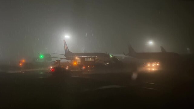 Planes and Service Vehicles in Foggy Rain. Atmospheric nighttime footage of a busy airport during heavy rain and fog. Silhouettes of airplanes and special equipment with flashing beacons in the light 
