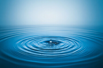A single water droplet creates gentle ripples in tranquil blue water, capturing the peace of early morning moments