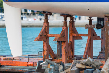 Boat hull maintenance with rusty stands in harbor setting