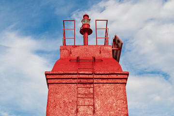 Red lighthouse tower against blue sky with ladder and light