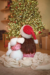 Back view of small  girl in red hat near the Christmas tree. The kid is waiting for a miracle on Christmas Eve. New Year's winter holidays