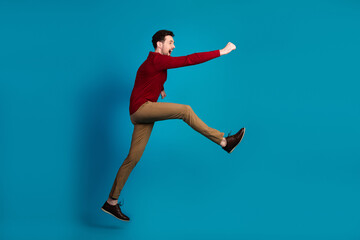 Young man in red sweater leaps with joy against blue background in a dynamic fashion lifestyle image