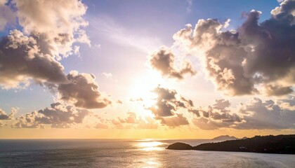 Fototapeta premium A beautiful sunset over the ocean, with dramatic clouds and an island in the distance. The sun is shining brightly, creating a warm and inviting atmosphere.