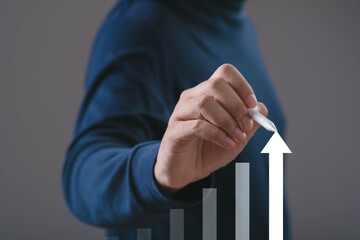 Hand drawing an upward arrow on a rising bar graph, symbolizing business growth, financial success, performance improvement, strategic planning, positive economic trends in a modern corporate context.