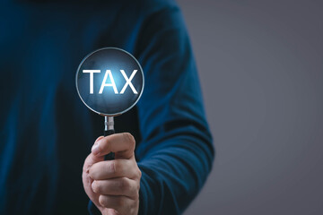 Hand holding magnifying glass highlighting the word TAX, representing tax analysis, financial review, auditing, compliance, and business decision-making in a modern economic and corporate context.