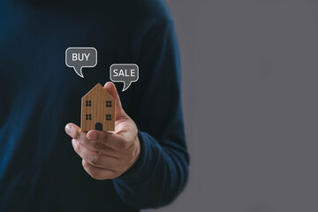 Hand holding wooden house model with buy and sale icons, symbolizing real estate marketing, property investment, housing market decisions, and home buying concepts in a modern business context.