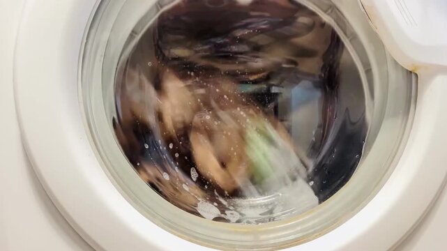  laundry tumbling and swirling behind the circular glass door of a modern washing machine with a steady hum sound