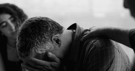 Man reacts emotionally during therapy session, eyes closed and mouth tense as another participant...