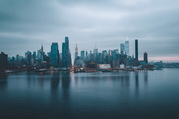 Fototapeta premium Modern city skyline reflected in calm water under moody sky