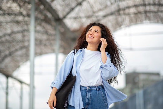 Joyful young Asian woman talking on phone while walking under metal structure