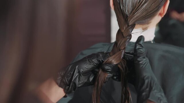 closeup braided hair being tightened, white woman client receives stylist attention as braid is smoothed and held for sleek finish, black gloved hands secure elastic and polish strands for neat