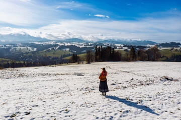 Female hiker with a backpack standing with her back to the camera, admiring the vast panorama of the snow-capped Tatra Mountains in winter. Travel and exploration concept.