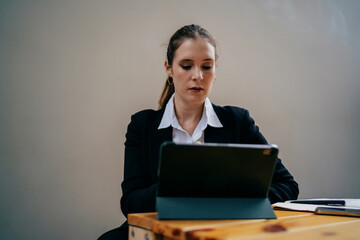 Businesswoman in black blazer looks down at digital tablet, fully immersed in remote task, conveying calm, discipline and personal engagement in digital freelance work environment