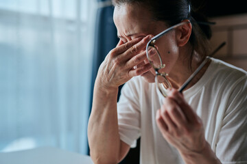 メガネを持ちながら目を押さえるシニア女性